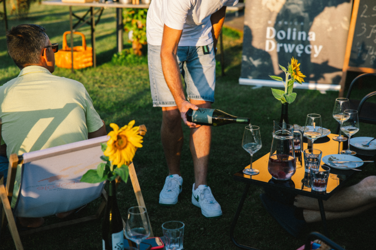 Wino nalewane gościom przy stolikach ze słonecznikami podczas spotkania w winnicy